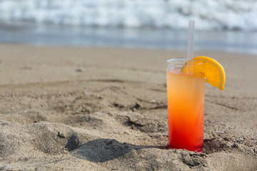 Glasses with colored cocktails on the beach with blue water in the background