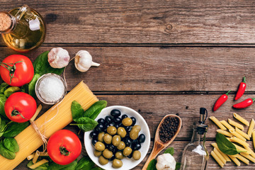 Raw ingredients for the preparation of Italian pasta, spaghetti, basil, tomatoes, olives and olive oil on wooden background. Top view. Copy space.