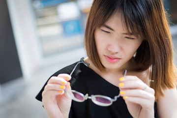 woman suffering from poor eye vision; portrait of asian woman with eye problem or bad blur eye sight holding eyeglasses, concept of seeing or visual disorder; young adult asian woman model