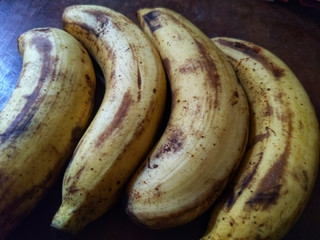 Four ripe bananas it have peels with yellow mixed a bit of brown put on the dark brown wooden table.