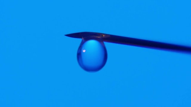 An arty macro of a crystalline droplet of liquid growing bigger and tumbling down at last. A water brooklet dribs after in a blue lab.