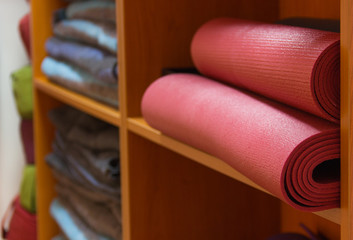 Fototapeta na wymiar Red yoga mats and blankets on wooden stand. Yoga equipment piled up on racks. Studio indoors, wellness center concept
