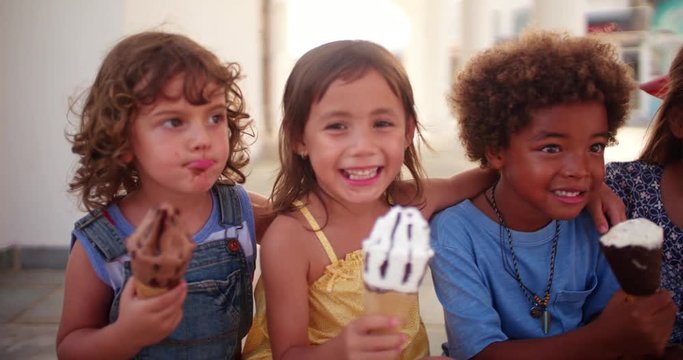 Multi-ethnic children eating ice-cream sitting on step outdoors in summer