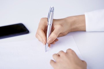 Closeup photo of businesswoman's hand holding pen and writing something while using mobile phone