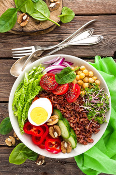 Buddha bowl dish with boiled egg, chickpea, fresh tomato, sweet pepper, cucumber, savoy cabbage, red onion, green sprouts, spinach leaves, walnuts, chia and rice