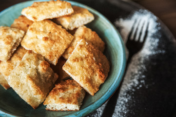 Appetizing picture of food, blue plate with a square home cookie on a background of a dark wooden table. Cookie structure. Sugar powder sprinkled with a fork
