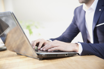 Close-up shot of businessman's hands while typing on keyboard. Professional man wearing suit while sitting at office desk and workin on laptop.