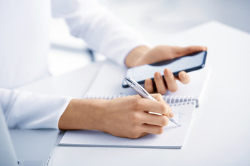Fototapeta premium Closeup photo of businesswoman's hand holding pen and writing something while using mobile phone