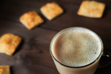 Appetizing picture of food, a cup with fragrant coffee, mocha, milk close-up against a dark wooden table. Structure of coffee foam. Clock from a square cookie