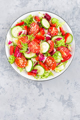 Fototapeta na wymiar Fresh vegetable salad with tomatoes, cucumbers, sweet pepper and sesame seeds. Vegetable salad on white plate