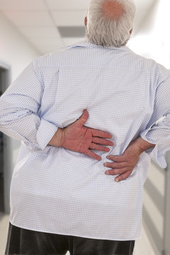 Overweight man with acute back ache bending over backwards to attenuate the pain, back view