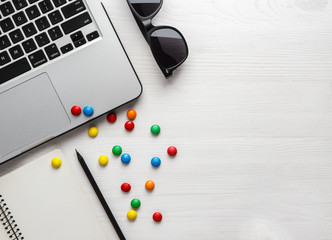 laptop, notebook with a pencil and colored candy on a white wooden background.