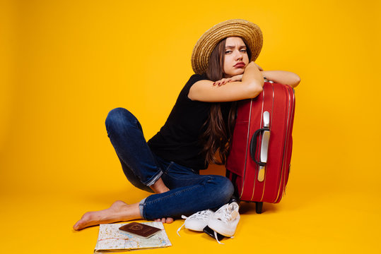 a sad disgruntled girl in a hat is waiting for her flight for a long time, goes on a trip with a big red suitcase