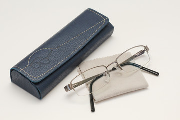 Glasses and case with glasses cleaning cloth on white wooden table