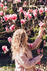 curly young woman walking in the park on a sunny day, standing next to a pink magnolia © mnelen.com