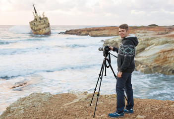 Young photographer with backpack making photos of sea and rocks with the camera. Mediterranean sea