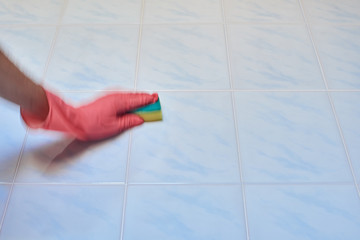 Closeup of hand in glove with sponge cleaning a tile in the bathroom