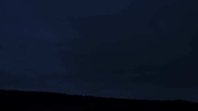 4K Time-Lapse. Paso de d&iacute;a a la noche pasando nubes r&aacute;pidamente sobre un bosque de pinos. Alemania.