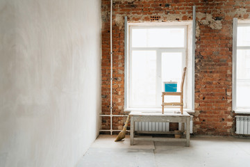 Fototapeta na wymiar concept repair. plaster of windows and walls of red brick. Large windows in the room, a construction goat, a chair and a bucket with putty.