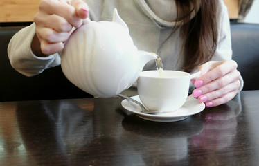 Close-up of the woman's hands pour tea from the teapot into a mug. Side view.