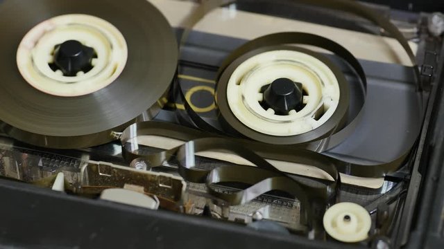 Audio tape loops and tangling in a deck cassette player when the take up spool stops or running slower than the other. Close up 4K static shot. Spinning magnetic tape in tape drive. 