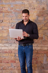 A serious handsome young businessman using a laptop PC in a black shirt.