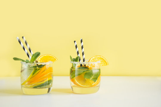 Two summer lemonade with lemon, orange and mint on yellow background.