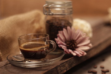 Portrait of a cup of coffee on a wooden board, with a flower and a container of coffee beans. Concept: Relax, breakfast, love