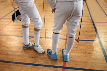 Girls, participants in fencing competitions on swords stand in the center of fencing hall waiting for beginning of the fight. Swords in their hands.