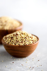 White and red raw organic quinoa in wooden bowl and rosemary on grey background. Healthy food ingredients. Copy space