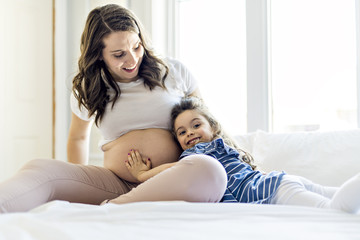 pregnant woman with her daughter on bedroom together