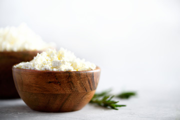 Homemade cottage cheese in wooden bowl, green rosemary on grey background. Copy space