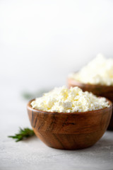 Homemade cottage cheese in wooden bowl, green rosemary on grey background. Copy space