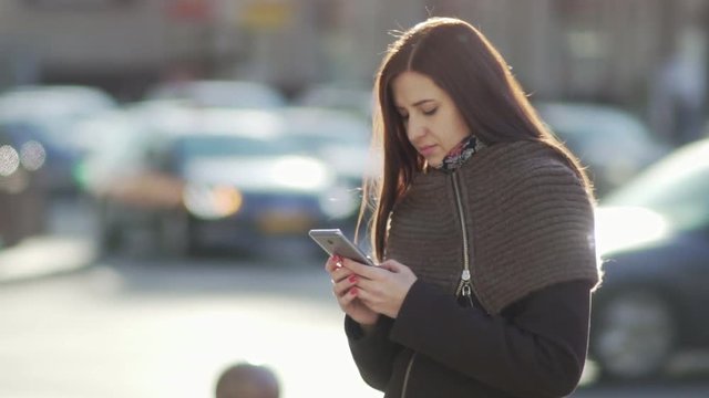 young attractive woman is using a smartphone in a big city at sunset against traffic background