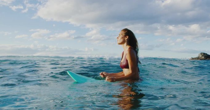 Beautiful young woman surfing at sunset