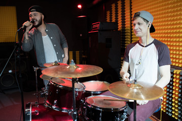 Portrait of modern hip-hop singer performing with his band in recording studio, drummer in foreground