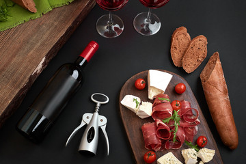 Obraz na płótnie Canvas Above overhead view flat lay still life of assortment various cheese and delicatessen with traditional bread and red wine on a old wooden board on black table