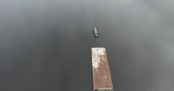 Top view of a river tug that pulls a rusty barge along a calm river. Summer day. The camera moves in the air near from the ship. Aerial view.