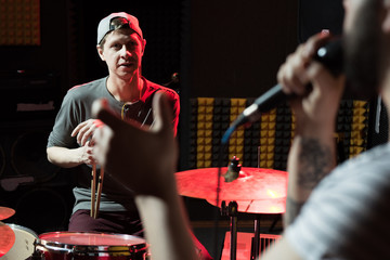 Portrait of modern hip-hop band rehearsing in recording studio lit by dim lights while making new...