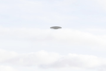 UFO Sighting, flying saucer in the white cloudy sky, metal reflective aircraft.