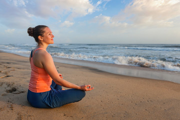 Fototapeta na wymiar Woman doing yoga oudoors at beach - Padmasana lotus pose
