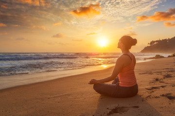 Woman doing yoga oudoors at beach - Padmasana lotus pose