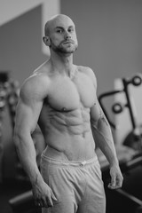 Shredded shirtless manful bodybuilder with beard posing in a gym. Fit man trains. Black and white portrait.