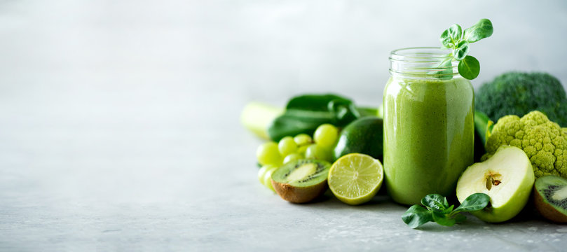 Glass jar mugs with green health smoothie, kale leaves, lime, apple, kiwi, grapes, banana, avocado, lettuce. Copy space. Raw, vegan, vegetarian, alkaline food concept. Banner