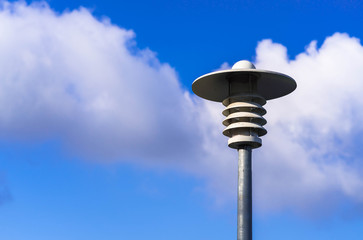 A modern lamppost in a public place against a blue sky and white clouds