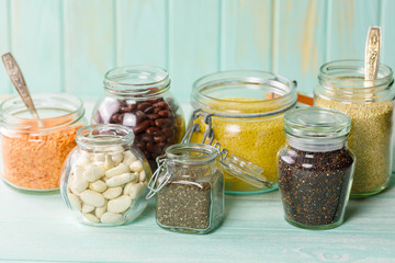 Fototapeta na wymiar White and red beans , chia seeds, various legumes, grains-beans, lentils, bulgur on concrete background in a glass jar with spoon on blue rustic old wooden background. 