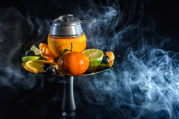 Modern fruit Hookah bowl with orange and a lot of fresh fruits with kaloud with red hot coconut coals charcoal with a lot of smoke at black background isolated. Smoking at dark shisha lounge