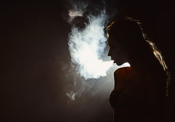 Beautiful young woman profile in backlight smoking hookah with a lot of smoke isolated black background. Club party menu concept