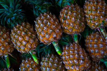 Rows of fresh pineapples diagonally on the market counter. Fruits with a branch in tropical Thailand. Asian diet. Texture.