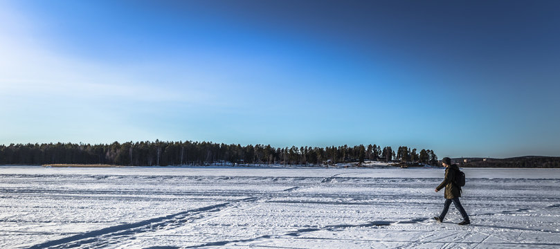 Falun - March 31, 2018: Traveler hiking on the frozen lake at Framby Udde near the town of Falun in Dalarna, Sweden